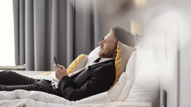 a business traveller laying on the bed listening to music on his earphones